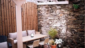 A patio area with a stone wall, wooden slats, wicker furniture, and string lights. - The Tailor Shop. (Skibbereen)