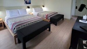 Habitación de hotel con dos camas, un escritorio y una mesita de noche.