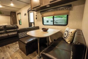A cozy RV interior with a dining area, seating, and a window with a view.