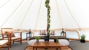 A tent interior with a bed, a wooden table, chairs, and small tables with lamps. - Deer Glamping Nordic Spa Access Near Grotto (Miller Lake)