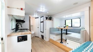 A compact RV interior with a kitchenette, seating area, and a window.