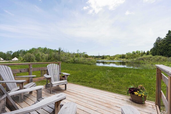 A wooden deck with Adirondack chairs overlooking a calm lake, surrounded by greenery.