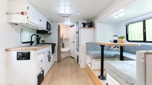 A compact RV interior with a kitchenette, a dining area, and a sleeping space.