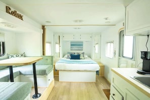 A compact RV interior with a bed, seating area, kitchenette, and a window. - Modern Glamping RV | Near Tobermory & Grotto (Miller Lake)