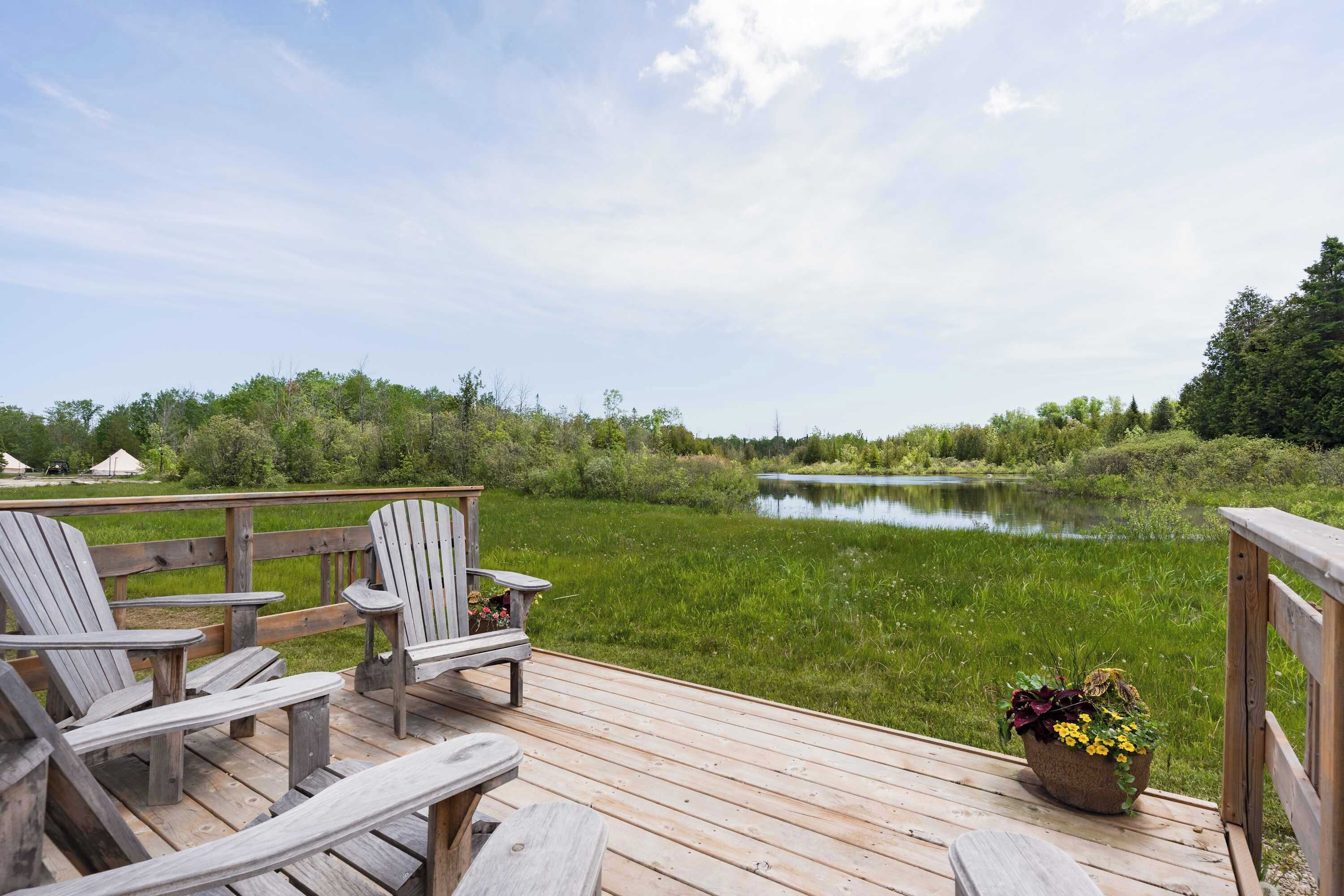A wooden deck with Adirondack chairs overlooking a calm lake, surrounded by greenery.
