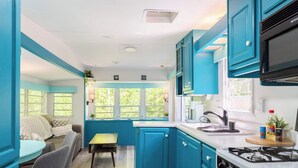 A compact kitchen with teal cabinetry, a dining area with a table and chairs, and a view through the window.