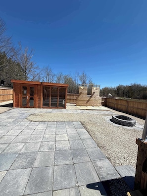 A wooden cabin with large windows, a stone fire pit, and a gravel patio.
