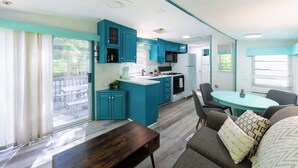 A modern kitchen with teal cabinetry, a central island, and a dining area with a round table and chairs.