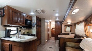 A compact RV kitchen with wooden cabinets, a microwave, and a sink.