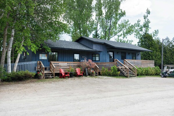 Un bâtiment à deux étages, avec une enseigne indiquant qu’il s’agit de bureaux, une allée gravillonnée, des bancs en bois et un véhicule de type voiturette de golf.