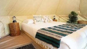 A tent-style bedroom with a bed, pillows, a blanket, a lantern, and a small plant. - Explorer Glamping Nordic Spa Access Near Grotto (Miller Lake)