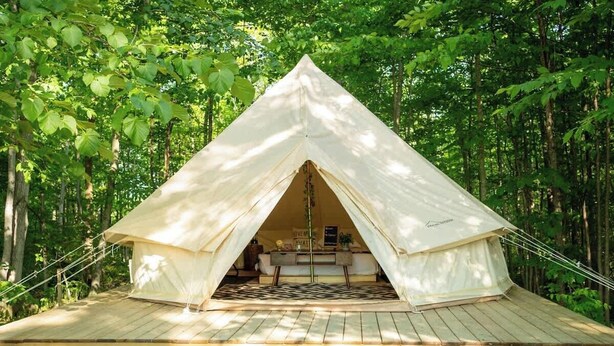A large, white, pyramid-shaped tent with a wooden deck in front, surrounded by dense forest. - Explorer Glamping Nordic Spa Access Near Grotto (Miller Lake)