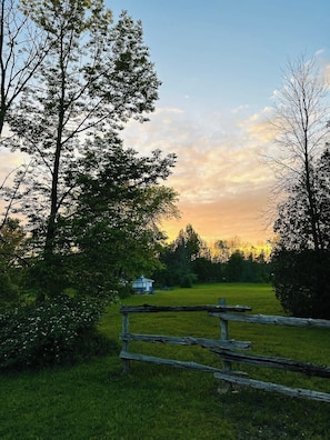 Un paysage rural avec une clôture en bois, un petit bâtiment et des arbres sous un ciel dégagé.