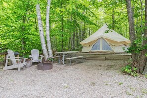 Una carpa con una mesa de picnic y sillas Adirondack en un bosque.