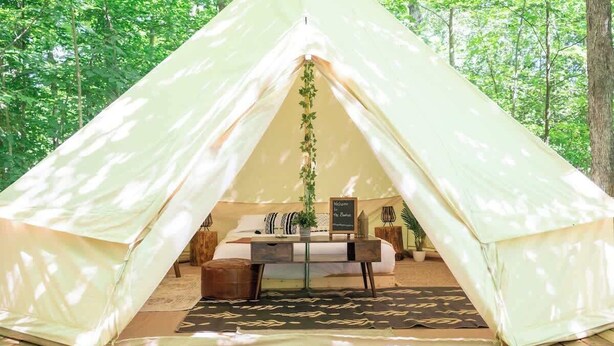 Ein Zelt mit Bett, umgeben von einem Wald.