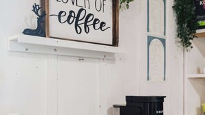 Ein Kaffee-Bereich mit einem Schild mit der Aufschrift 'LOVER OF coffee', einer Kaffeemaschine und einer Kaffeetassen-Serviertablett.