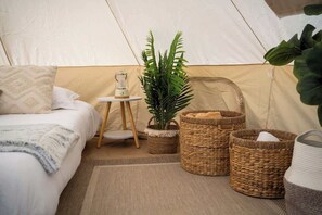 A tent interior with a bed, a small table, a plant, and woven baskets.
