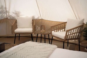 Una carpa con dos sillas de mimbre, una mesita pequeña, una manta blanca y un tapiz tejido.