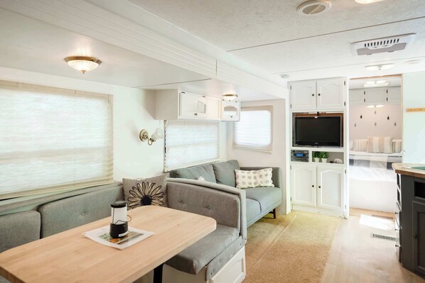 A compact RV interior with a kitchenette, seating area, and a television.