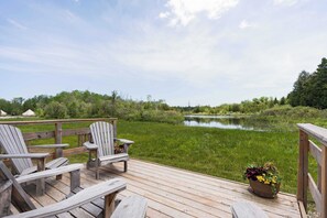 A wooden deck with Adirondack chairs overlooking a calm lake, surrounded by greenery.