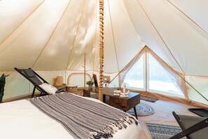 A tent with a bed, two chairs, a small table, and a window.