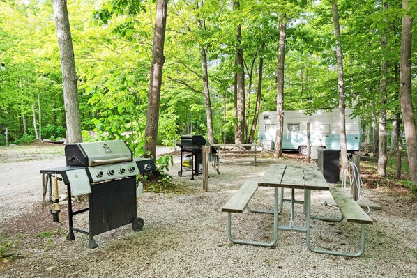 A campsite with a grill, picnic table, and RV.