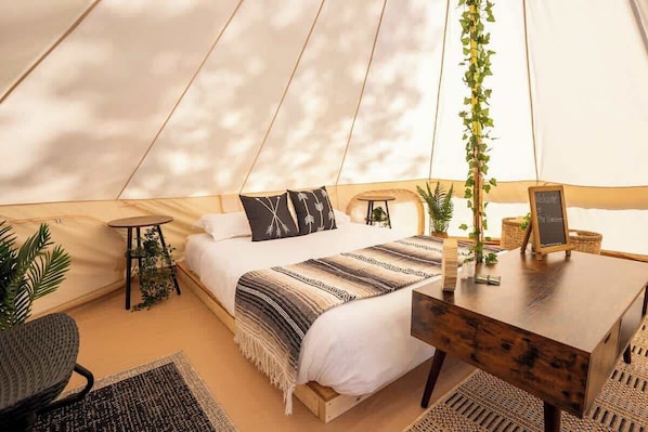 A tent-style room with a bed, a wooden table, a small round table, and a chair.