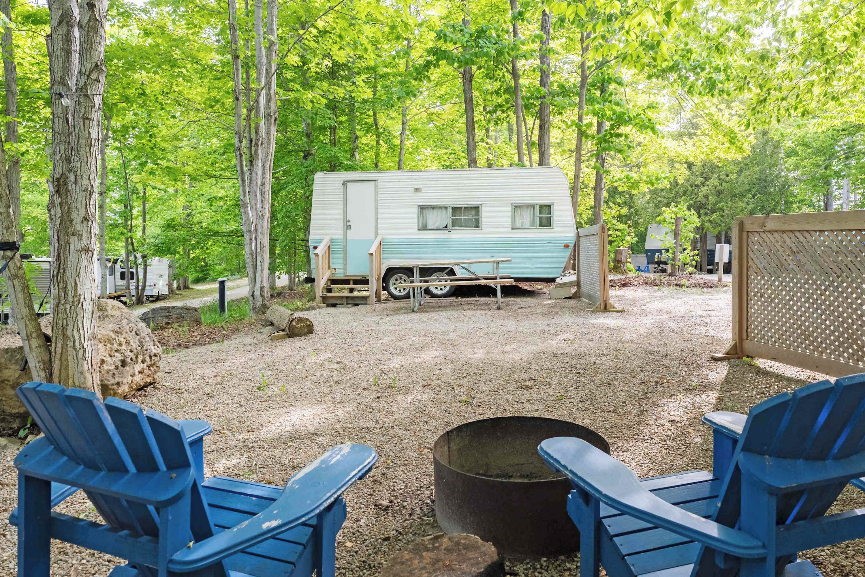 A campsite with a trailer, two blue chairs, and a fire pit.