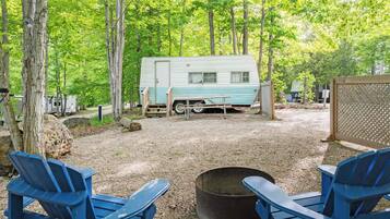 A campsite with a trailer, two blue chairs, and a fire pit.