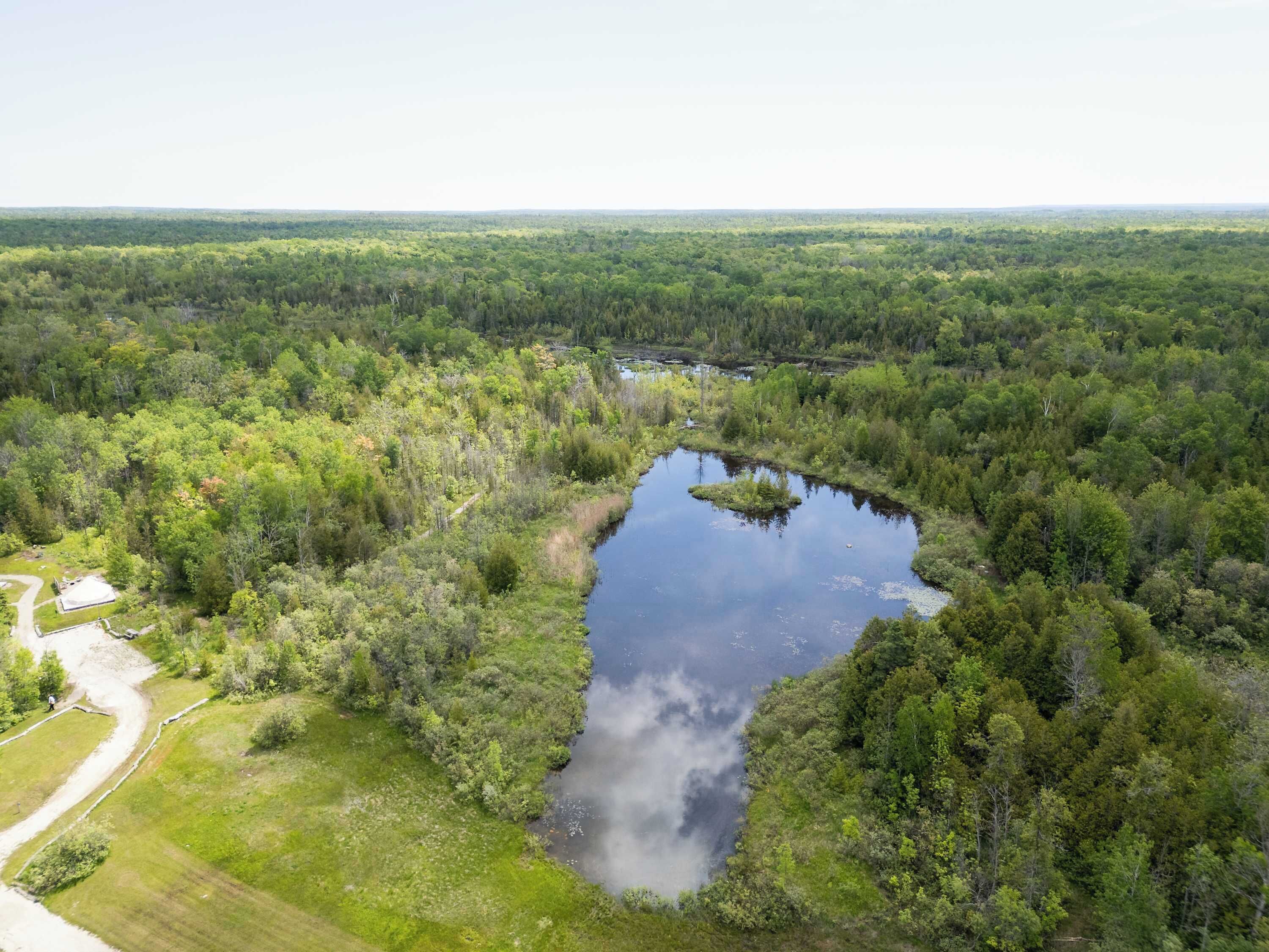 An aerial view of a forested area with a winding river, a clear sky, and a small building with a paved area.