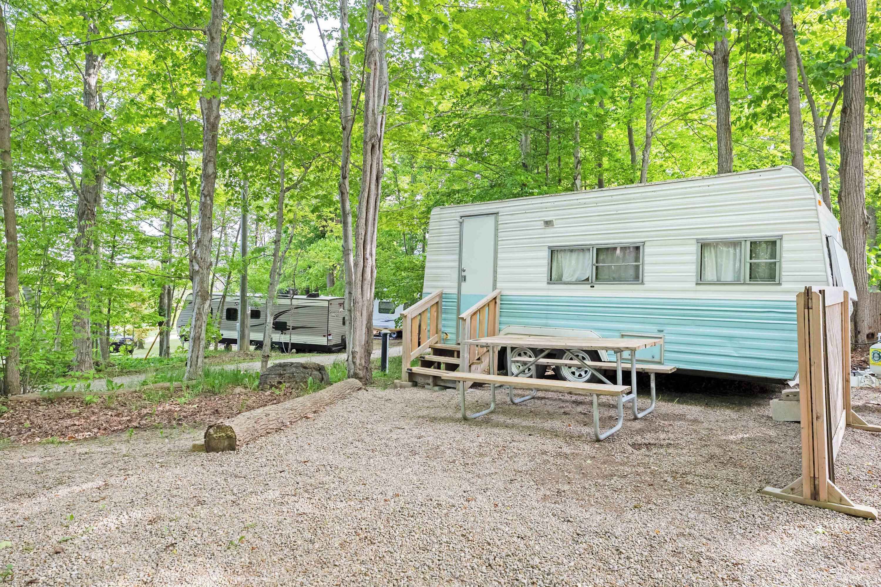 A recreational vehicle (RV) campsite with a gravel ground, a picnic table, and a wooden bench.