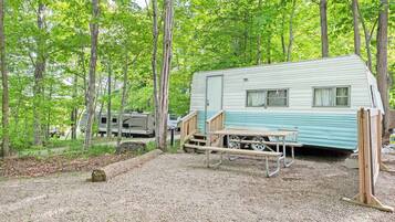 A recreational vehicle (RV) campsite with a gravel ground, a picnic table, and a wooden bench.