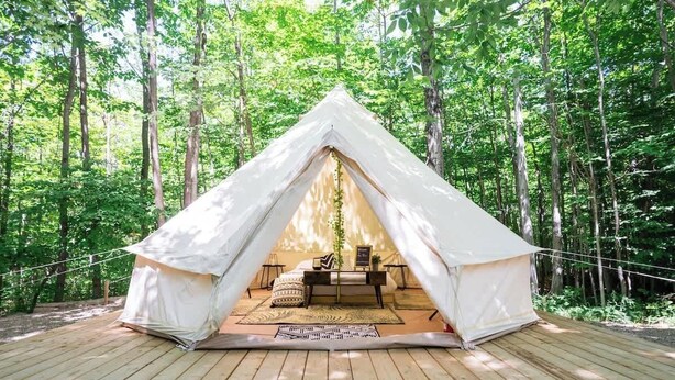 Una carpa blanca con una terraza de madera, rodeada de árboles.