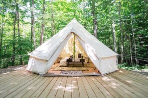 A white tent with a wooden deck, surrounded by trees.