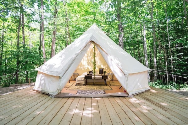 A white tent with a wooden deck, surrounded by trees.