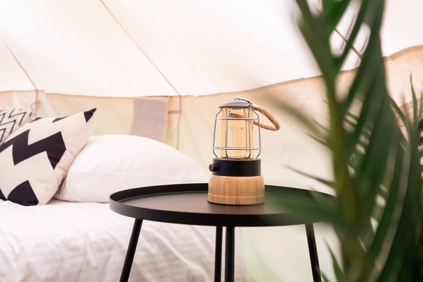 A portable lantern on a round table in a tented accommodation.
