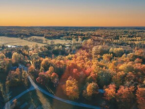 Luchtbeeld van een landschap met herfstkleuren, wegen en verspreide gebouwen.