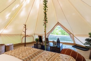 A tent interior with a bed, a small table, a hanging plant, and a view of the outdoors. - Boho Glamping Nordic Spa Access Near Tobermory (Miller Lake)