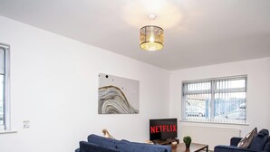Ein Wohnzimmer mit einer Couch, einem Fernseher, einem Gemälde und einem Fenster mit Blick auf geparkte Autos.