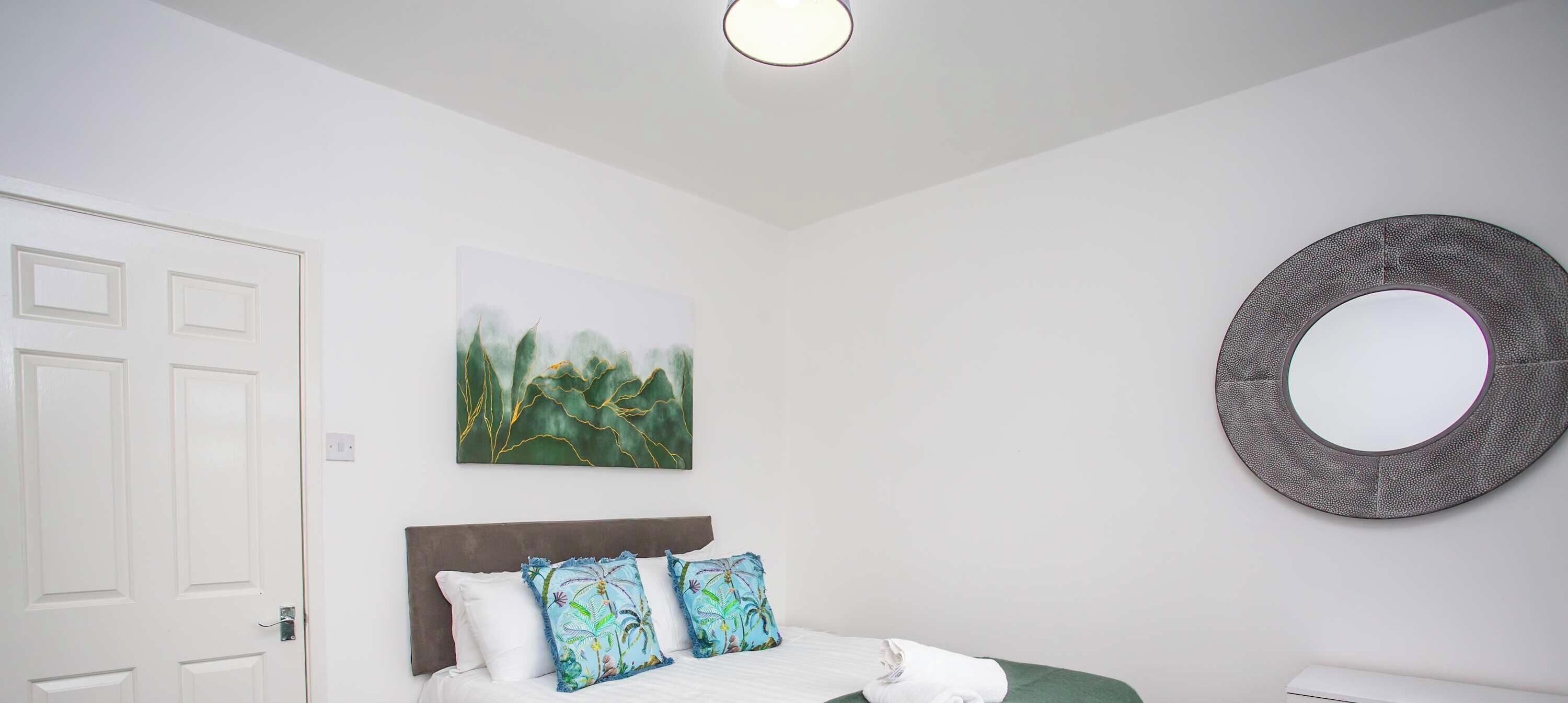 A bedroom with a bed, a round mirror, and a painting on the wall.