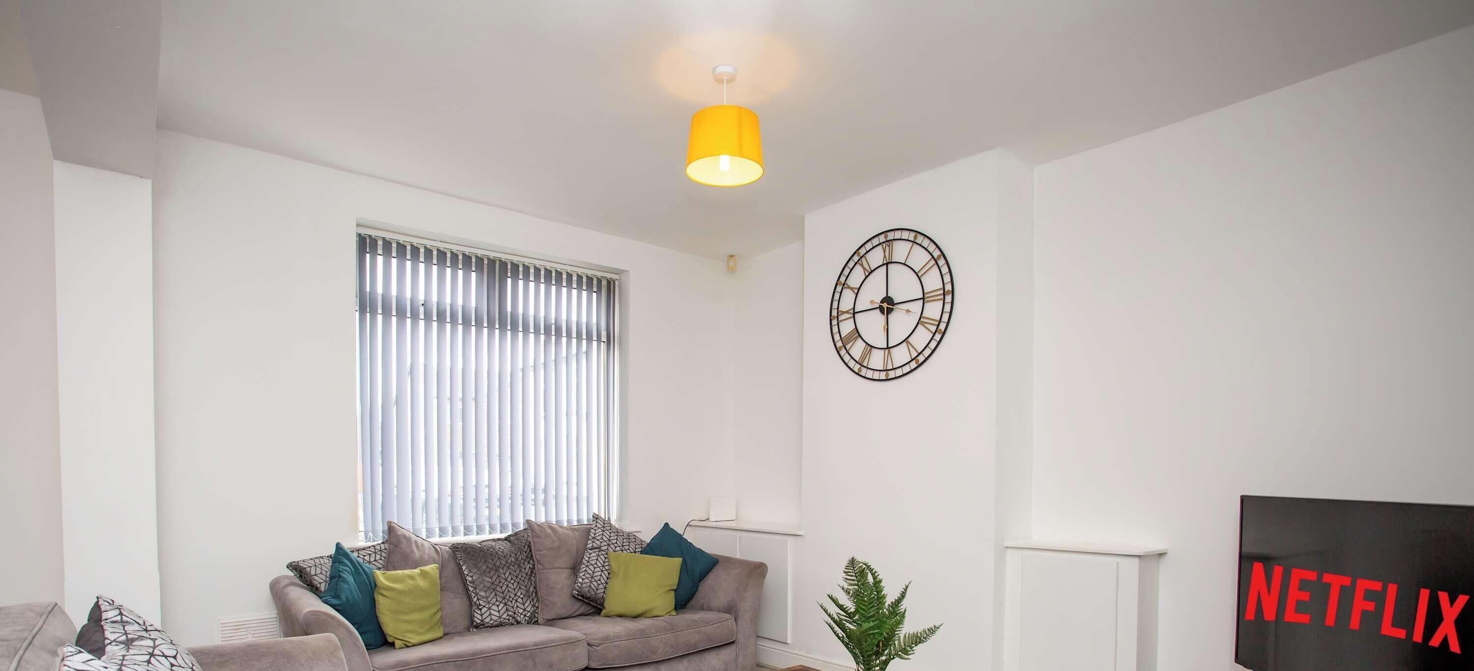 A living room with a sofa, a plant, a wall clock, and a Netflix sign.