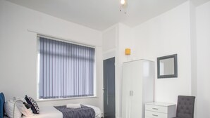 Um quarto com cama, mesa de cabeceira, guarda-roupa, espelho e janela com persianas.