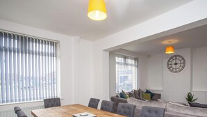 Uma sala de estar moderna com uma mesa de jantar de madeira, sofá cinza estofado e uma televisão grande exibindo o logotipo da Netflix.