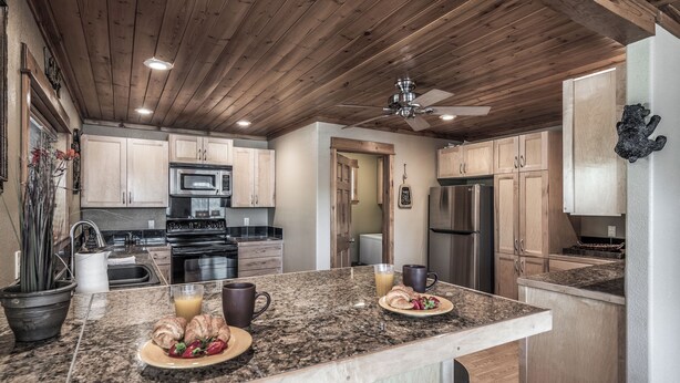 A kitchen with granite countertops, wooden cabinets, stainless steel appliances, and a ceiling fan. - Double Elk Lodge by Ruidoso Vacation Rentals (Ruidoso)