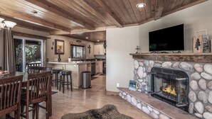 A spacious living area with a stone fireplace, wooden ceiling, and a large flat-screen TV mounted above it. - Double Elk Lodge by Ruidoso Vacation Rentals (Ruidoso)