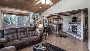 A spacious living room with a large brown leather sofa, a black ottoman, and a stone fireplace. - Double Elk Lodge by Ruidoso Vacation Rentals (Ruidoso)