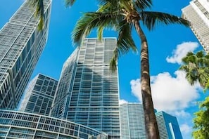 A modern high-rise building with a curved glass facade, surrounded by palm trees and clear blue sky.