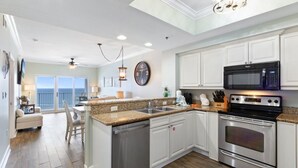 A modern kitchen with white cabinets, stainless steel appliances, a granite countertop, and a view to the outside. - Seawind 1502 | Beach Front (Gulf Shores)