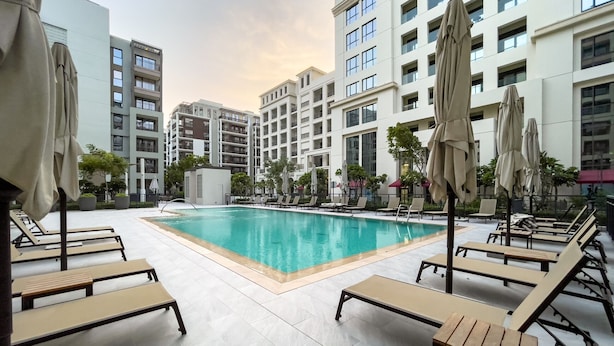 Una piscina con sillones de descanso y sombrillas, rodeada de edificios altos.