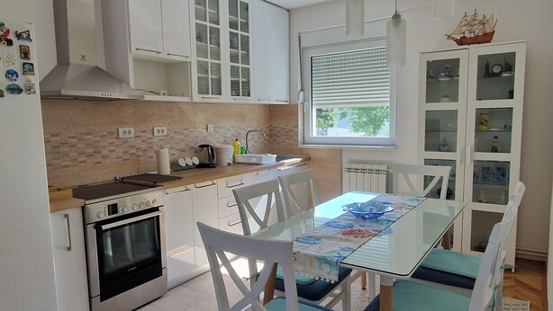 A modern kitchen with white cabinets, a built-in oven, and a dining area with a glass table and white chairs.